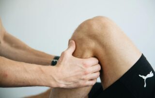 Hands examining a patient's knee joint during an orthopedic assessment.
