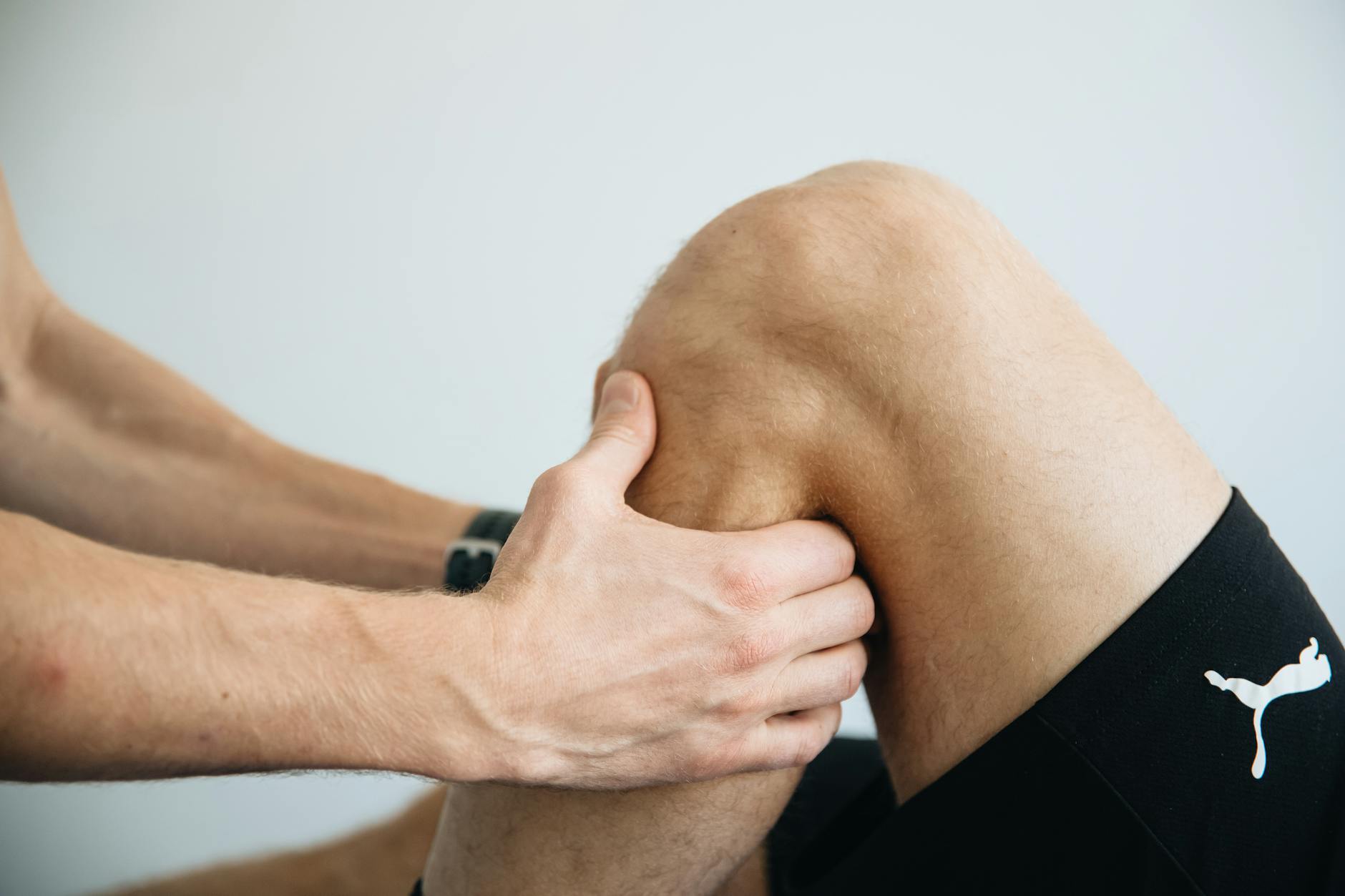 Hands examining a patient's knee joint during an orthopedic assessment.