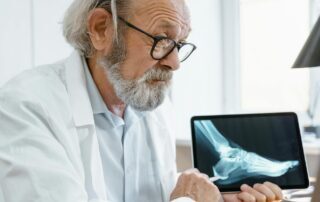 Elderly orthopedic doctor in white coat examining a foot X-ray on a digital tablet.