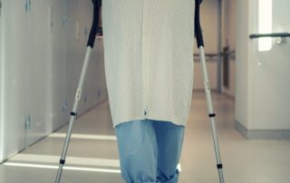 Senior patient using crutches to walk down a hospital corridor during hip replacement recovery