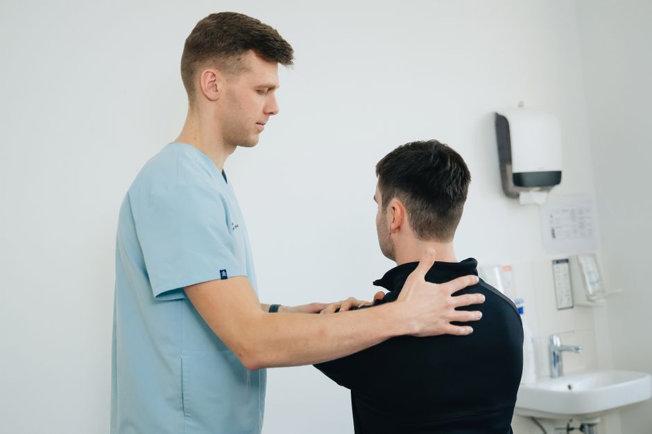Physiotherapist examining a patient's shoulder in a clinical setting for rotator cuff assessment.