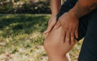 Person clutching painful knee outdoors, illustrating knee pain from spring yard work in Treasure Valley.
